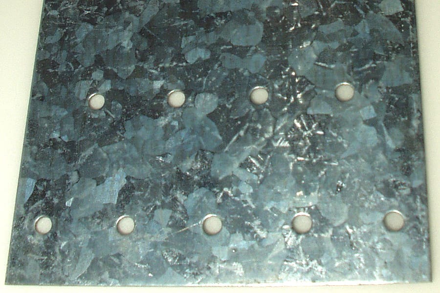 A grey metal plate with holes, its surface covered in a shiny crystal pattern like large flakes