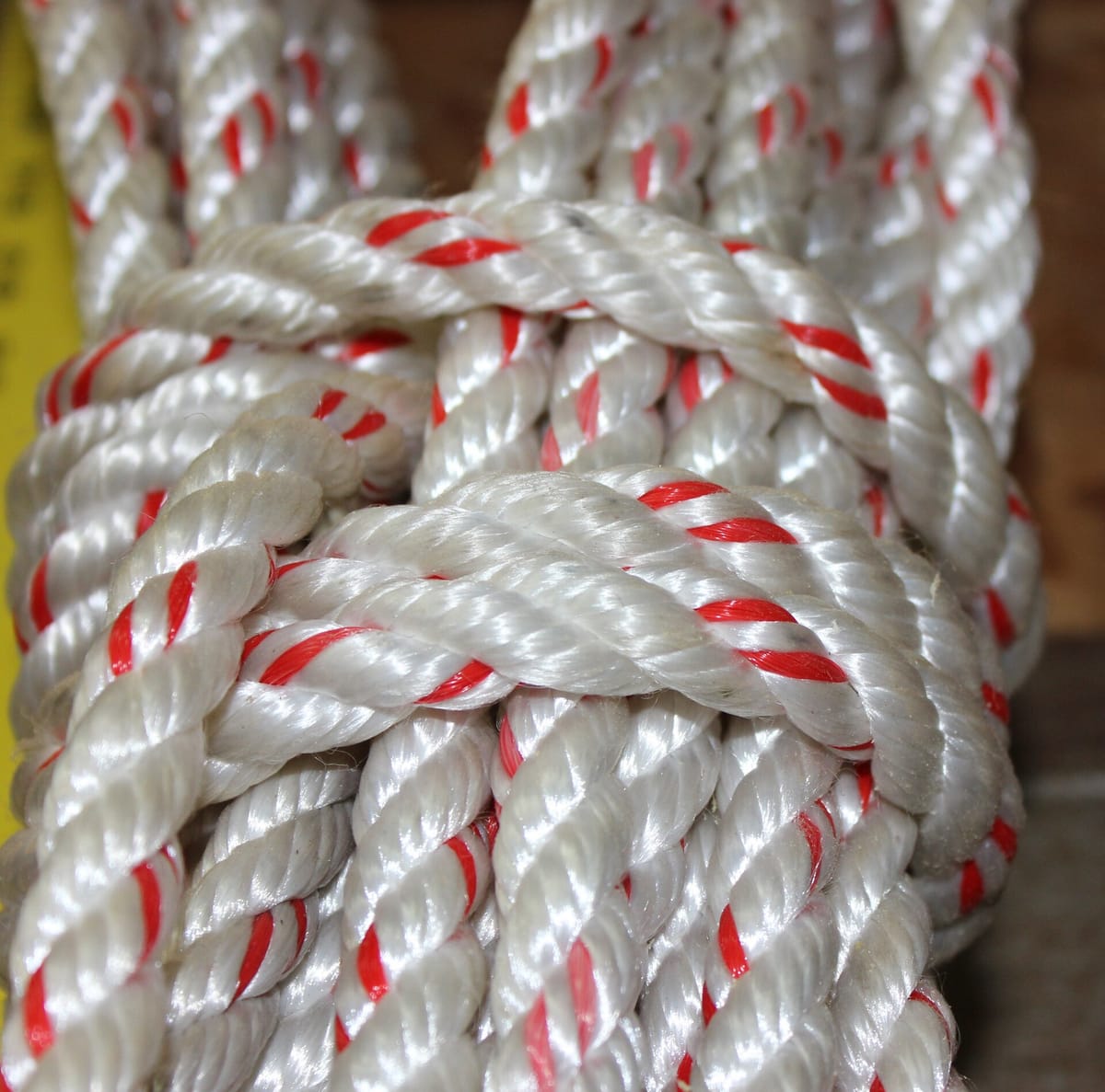 Close-up of a thick white twisted rope with a red tracer strand, tied in a knot
