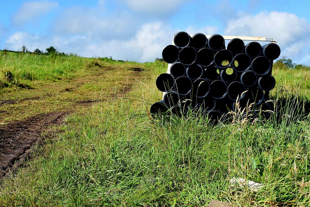 A stack of black plastic pipes seen end-on, lying in a grassy field