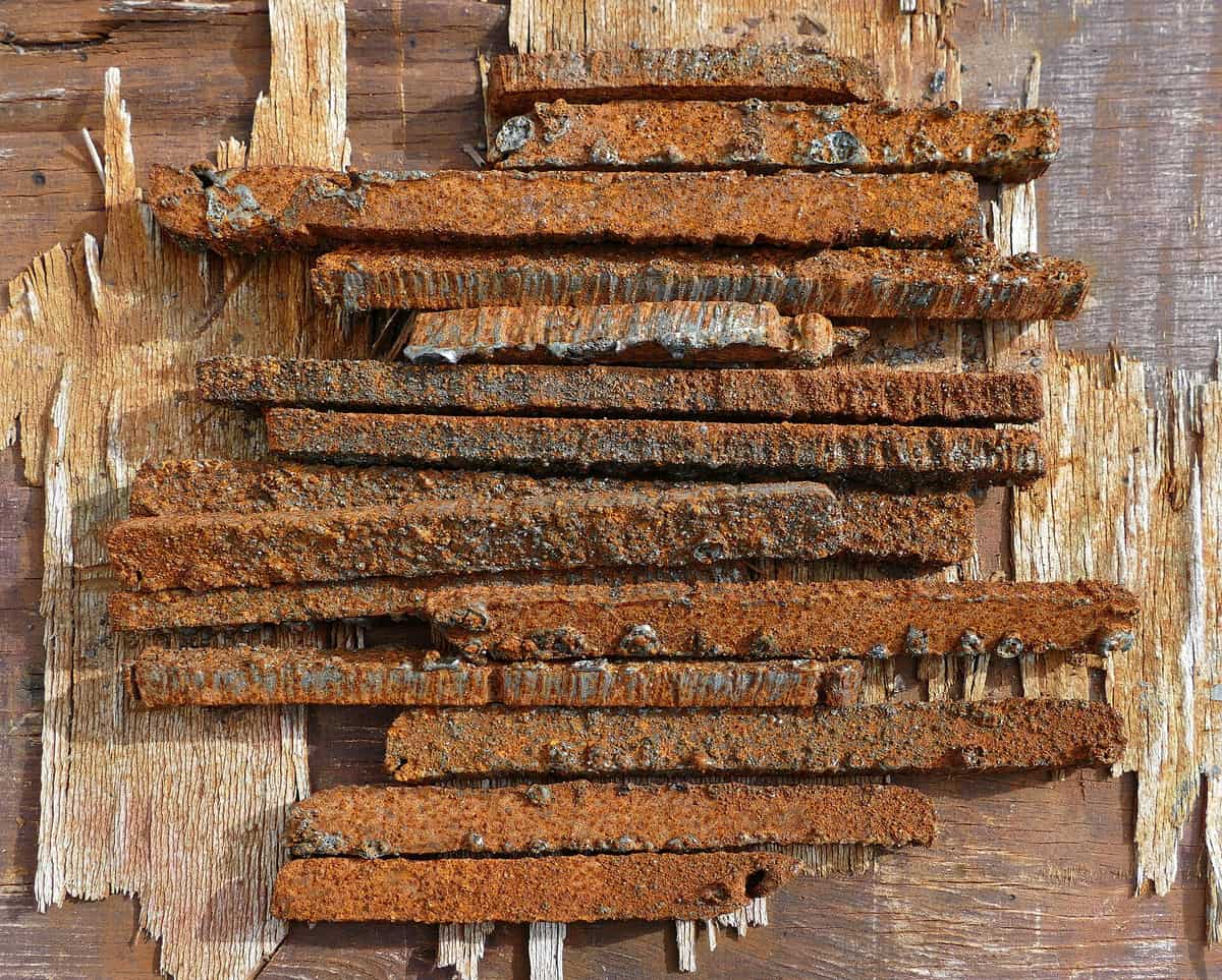 A pile of flat iron strips covered in rough orange-brown rust, lying on old weathered wood