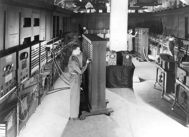 A long room lined with ENIAC's tall panels of switches and cables