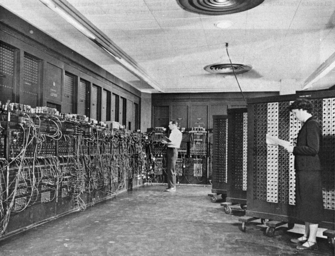 Two programmers setting cables and switches on the large panels of the ENIAC computer