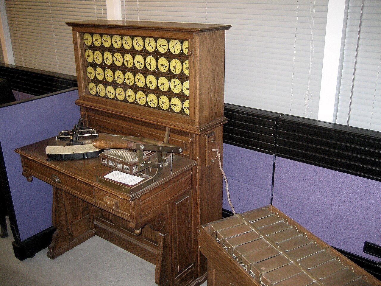 A wooden desk machine with rows of round dials and a sorting box beside it