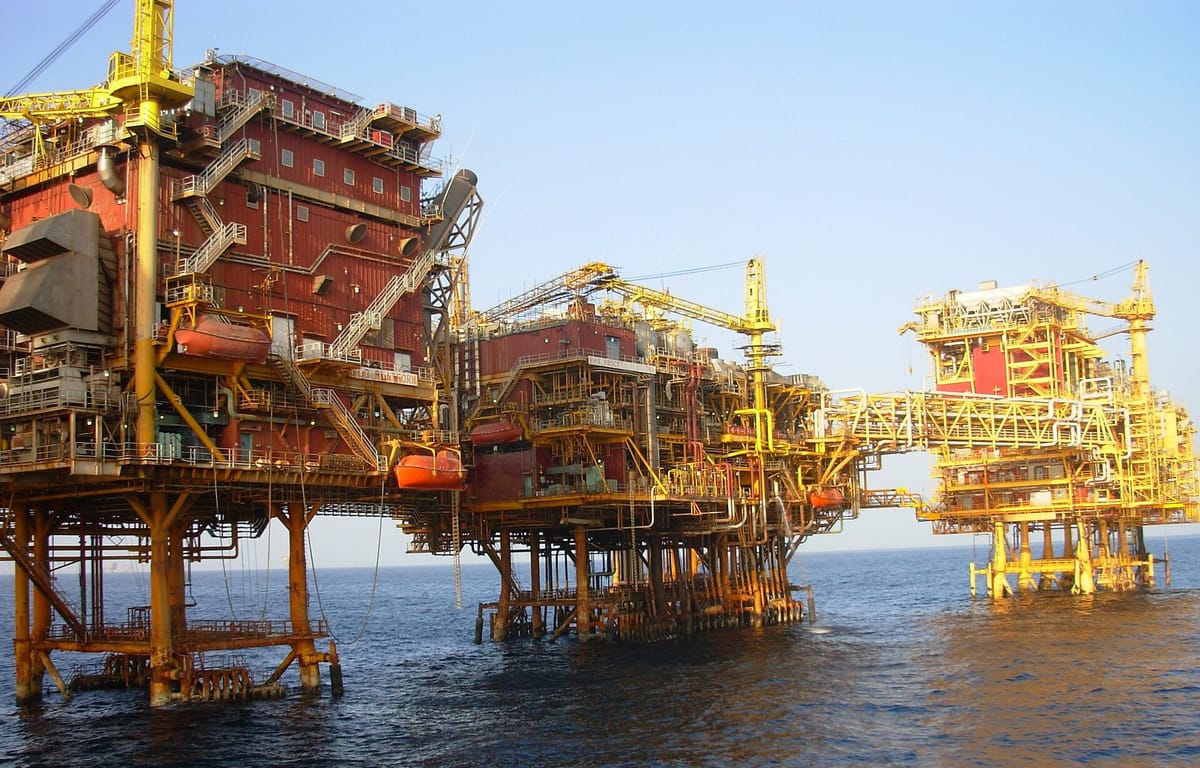 Several large red and yellow steel oil platforms standing on legs in the open sea, joined by long bridges, with orange lifeboats hanging on their sides