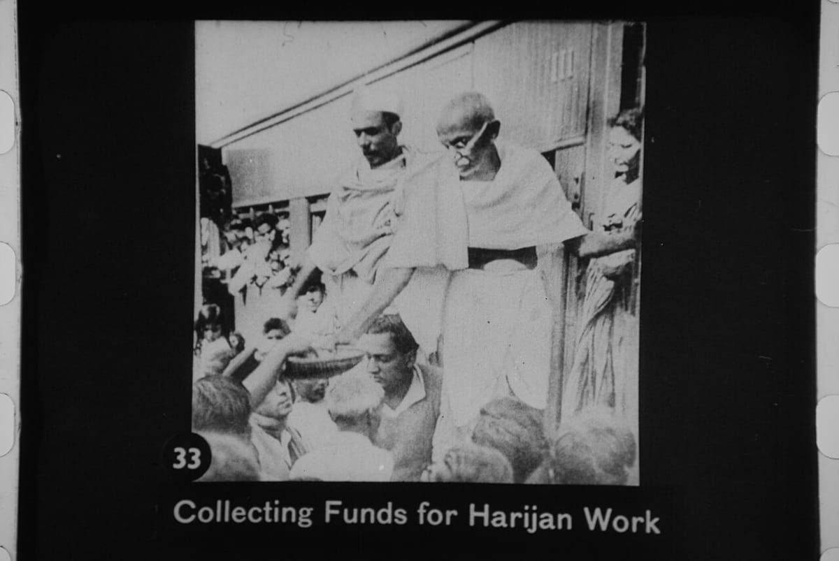 1930 ਦੇ ਦਹਾਕੇ ਵਿੱਚ ਲੋਕਾਂ ਵਿਚਕਾਰ ਬੈਠੇ ਮਹਾਤਮਾ ਗਾਂਧੀ ਭੀੜ ਤੋਂ ਪੈਸੇ ਇਕੱਠੇ ਕਰਦੇ ਹੋਏ