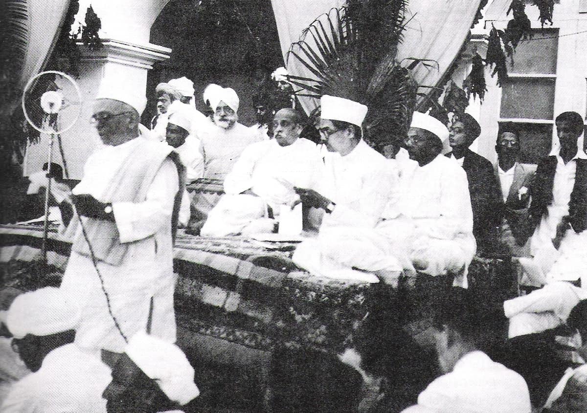 Old black-and-white photo of three men in white clothes and caps at a public ceremony