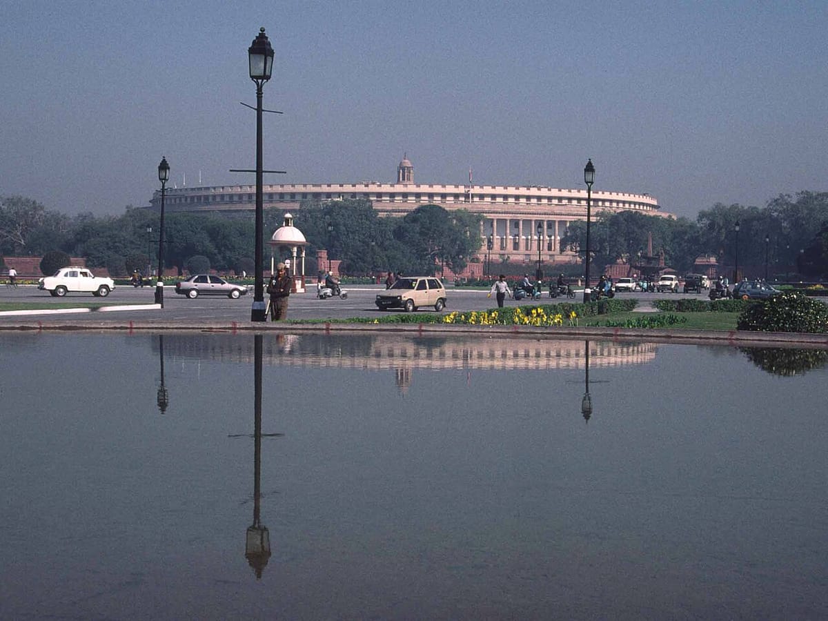 The circular old Parliament House with its long row of pillars reflected in a pool of water