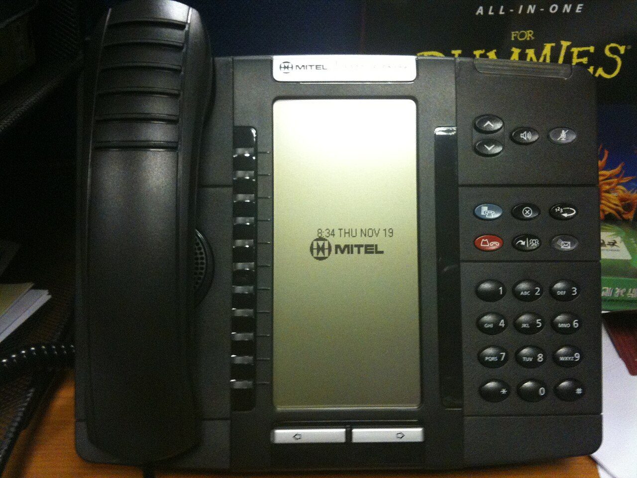 A grey office desk phone with a small screen and rows of buttons