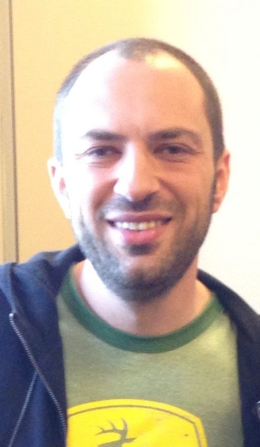 Jan Koum smiling, with short hair and stubble, in a dark hooded jacket