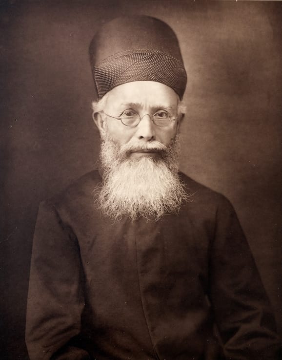 Old portrait of Dadabhai Naoroji with a white beard and a Parsi cap
