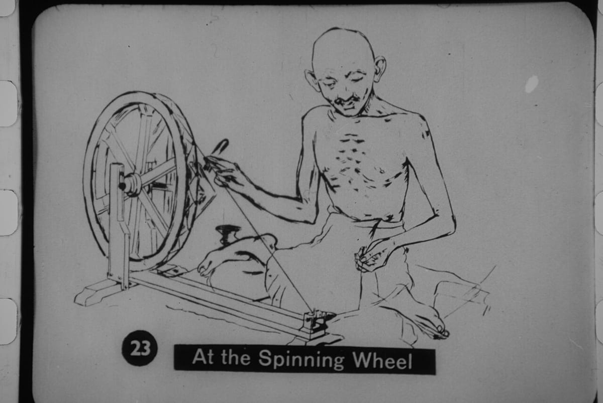 Old photograph of Gandhi sitting on the floor and spinning at a charkha