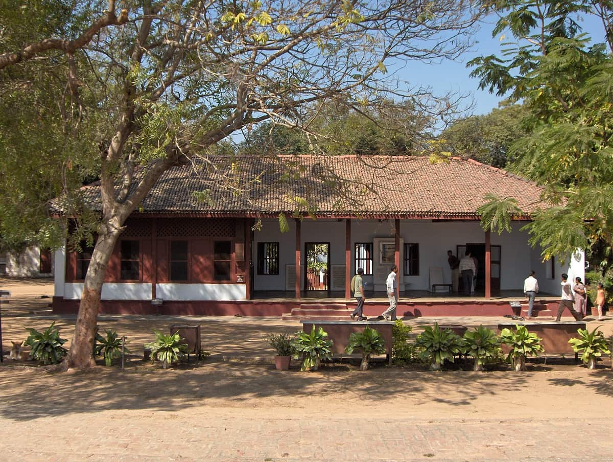 Front of a simple white single-storey house with a tiled roof and a verandah at the Sabarmati Ashram