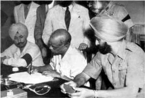 ਮੇਜ਼ ਉੱਤੇ ਬੈਠ ਕੇ ਦਸਤਾਵੇਜ਼ ਉੱਤੇ ਦਸਤਖ਼ਤ ਕਰਦੇ ਵੀ. ਪੀ. ਮੈਨਨ