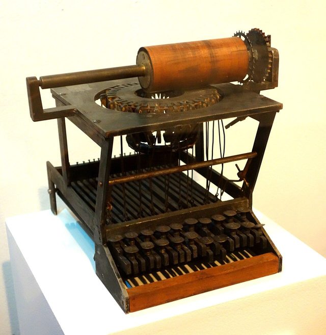 An early wooden and metal typewriter with round keys, on display in a museum