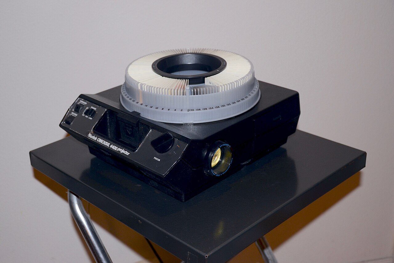 A grey Kodak Carousel slide projector with a round slide tray on top