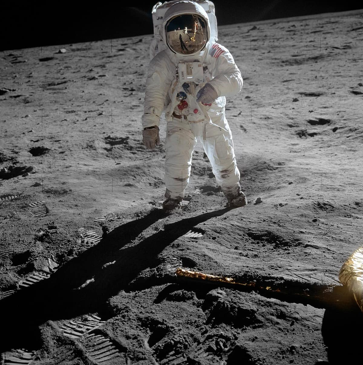 An astronaut in a white spacesuit with a gold visor standing on the grey, dusty surface of the Moon