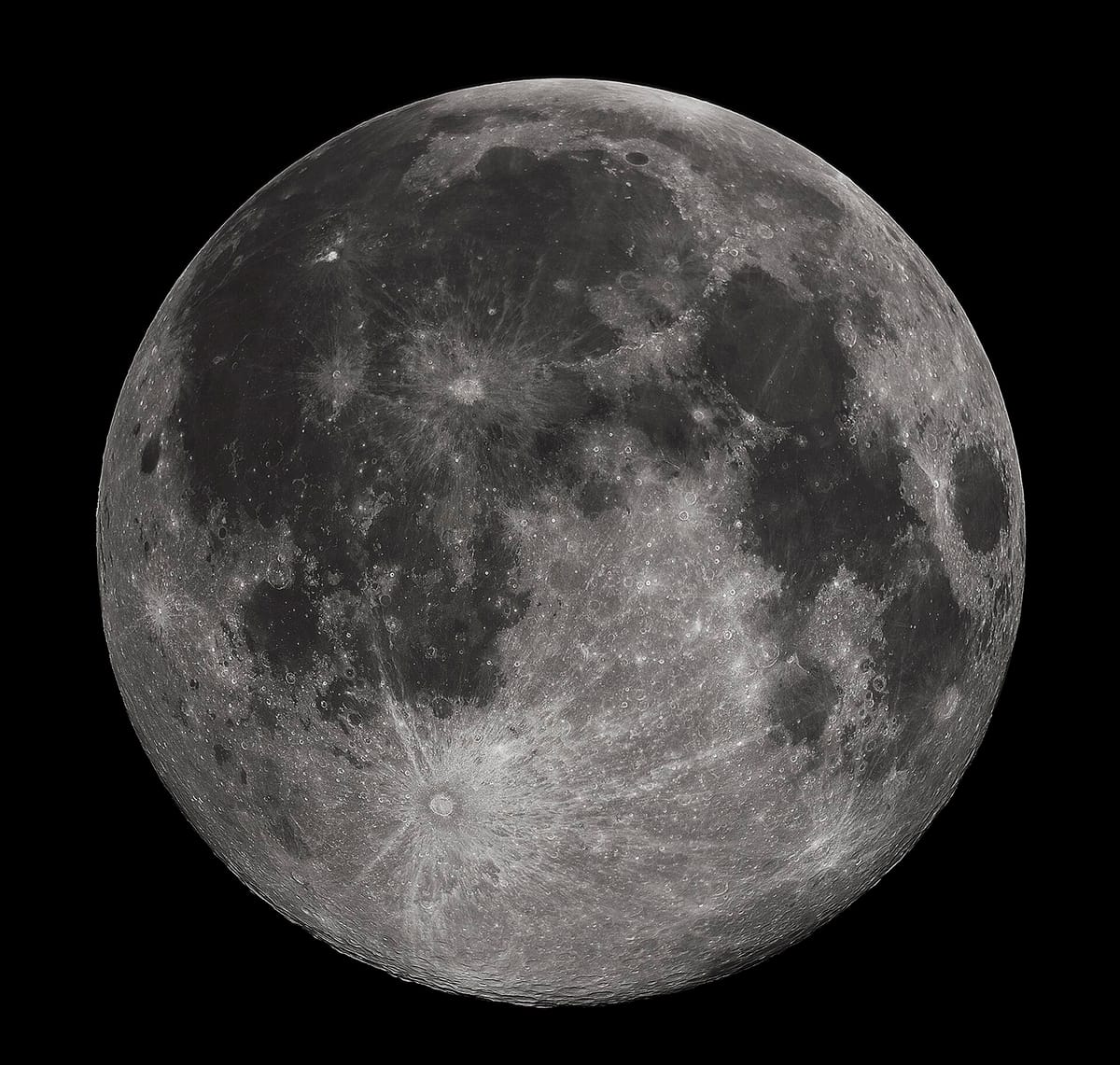 The full Moon in grey and white, with dark patches and bright rayed craters, on a black sky