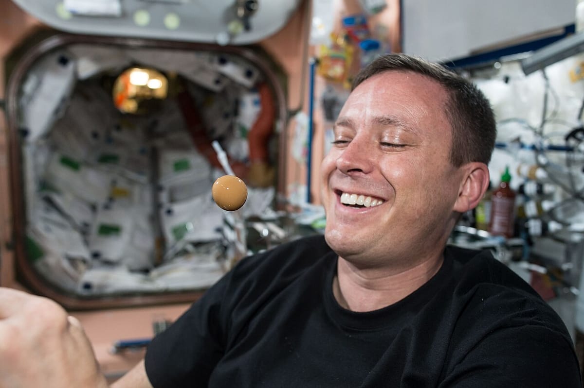 An astronaut inside the space station watching a round ball of liquid floating in the air in front of his face