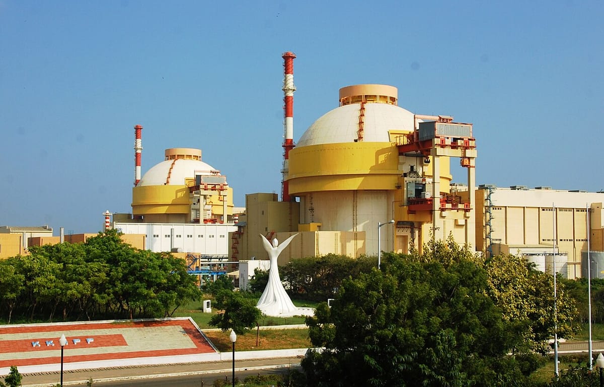 Two large reactor buildings with white domes and yellow walls, red-and-white chimneys, trees and a white statue in front