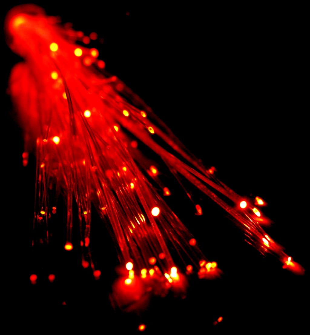 A bundle of thin glass threads glowing red against a black background, with bright dots of light at their tips