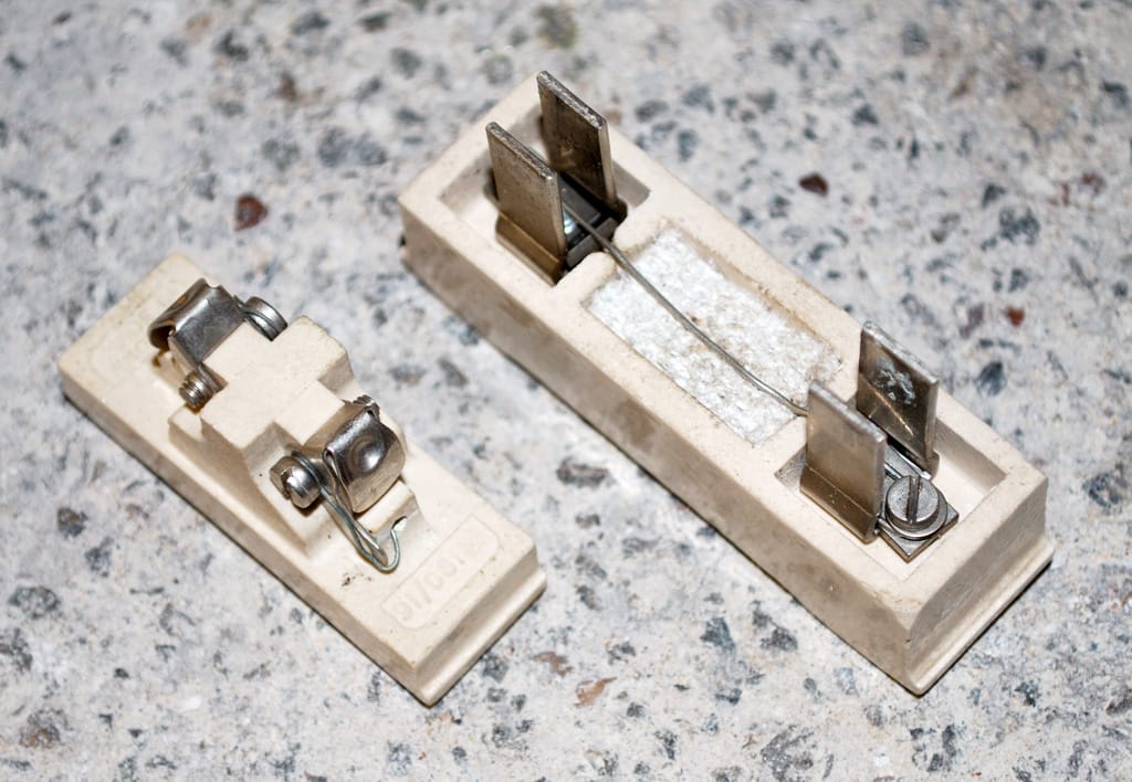 Two white porcelain parts of a rewirable fuse on a stone floor, with metal contacts and a thin fuse wire fixed between screws