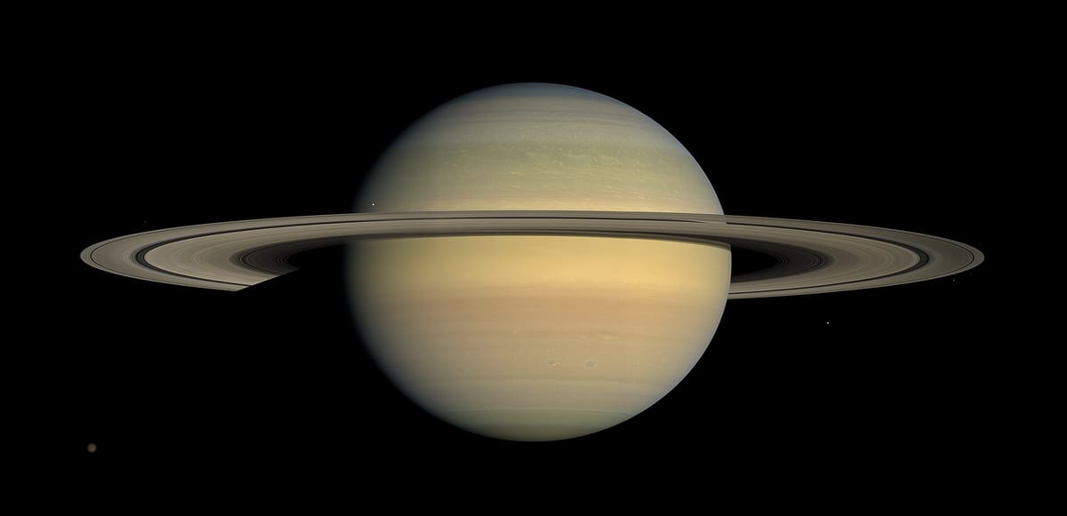 Saturn, a pale yellow banded planet, with its wide flat rings seen almost edge-on