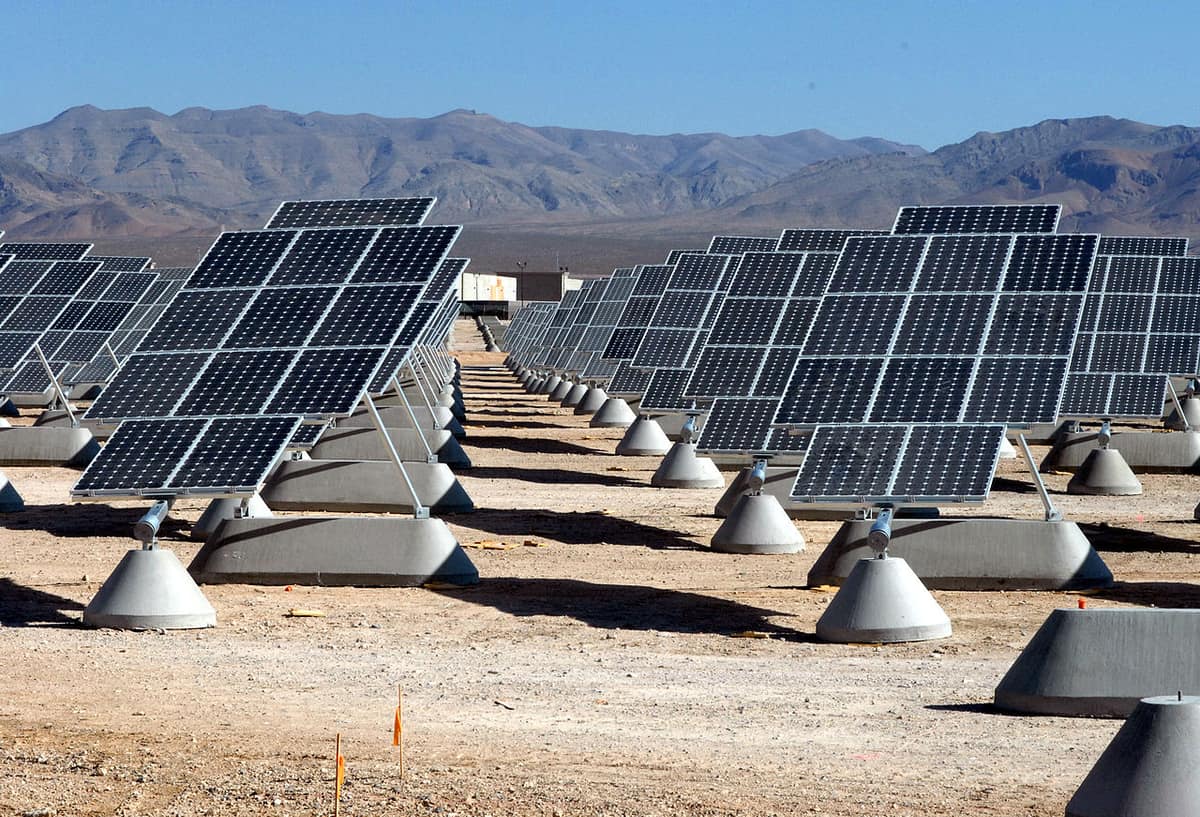 Rows of dark blue solar panels on concrete stands in a desert, with bare mountains behind