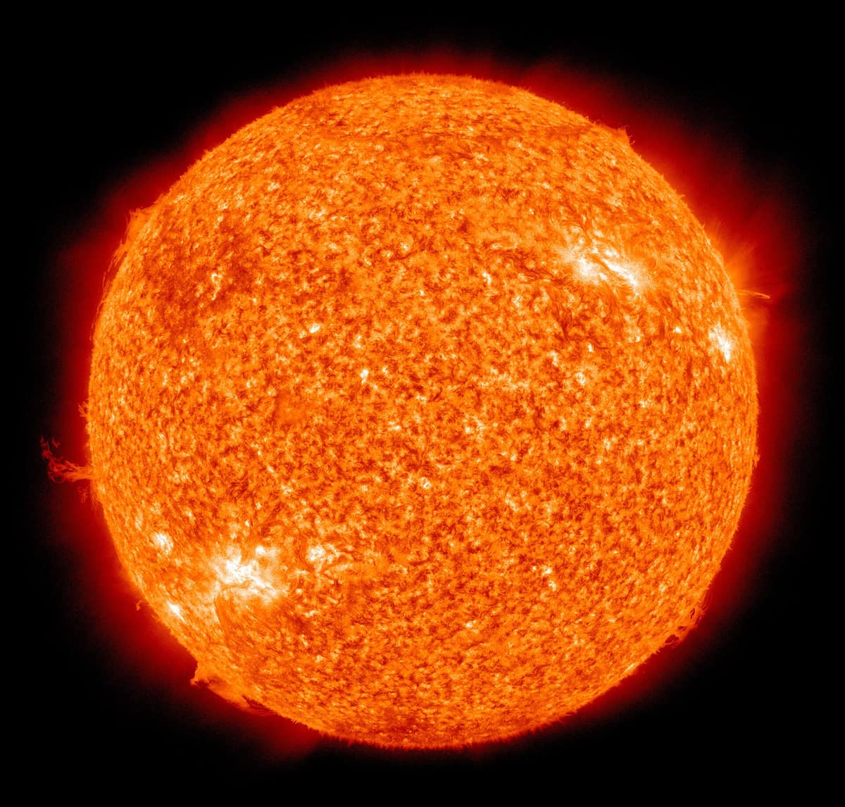The whole Sun as a glowing orange ball with bright patches and loops of gas at its edge, on a black background