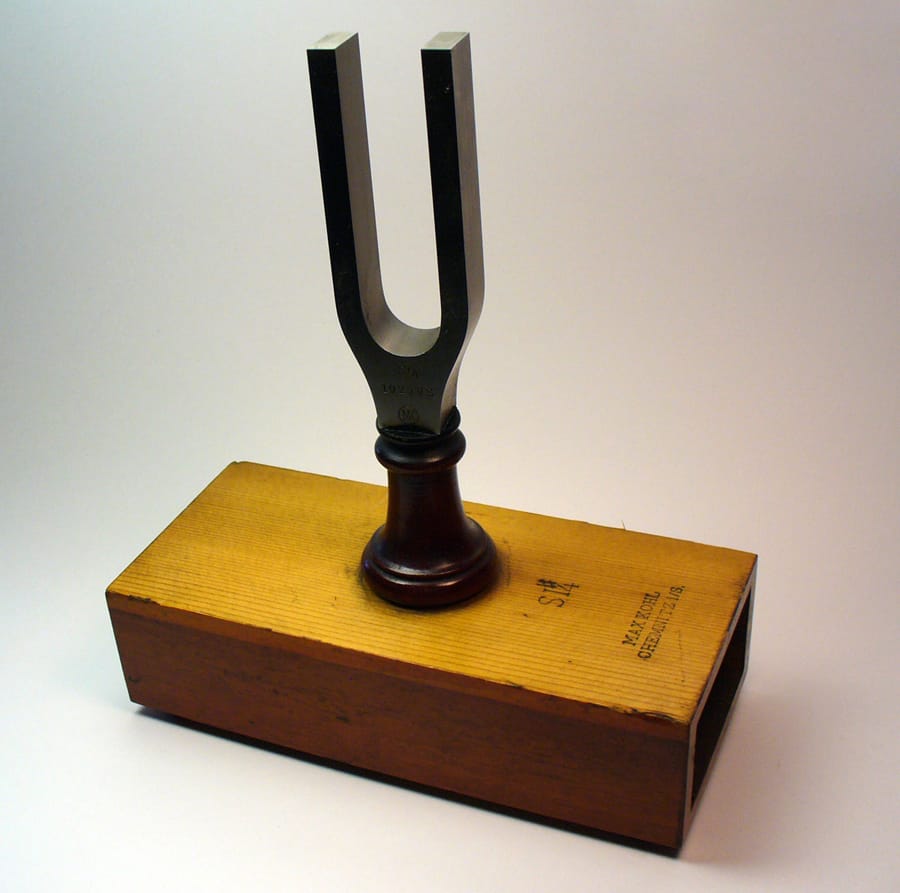 A steel tuning fork standing upright on a hollow wooden box