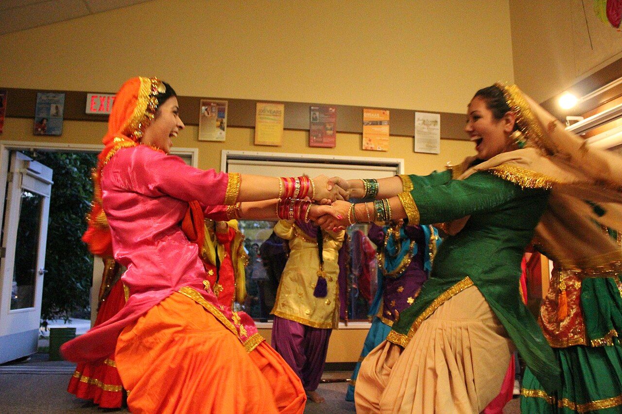 ਤੀਆਂ ਦੇ ਜਸ਼ਨ ਵਿੱਚ ਰੰਗਦਾਰ ਸੂਟਾਂ ਅਤੇ ਸੁਨਹਿਰੀ ਕਿਨਾਰੀ ਵਾਲੀਆਂ ਚੁੰਨੀਆਂ ਵਿੱਚ ਹੱਥ ਫੜ ਕੇ ਹੱਸਦੀਆਂ-ਘੁੰਮਦੀਆਂ ਦੋ ਔਰਤਾਂ