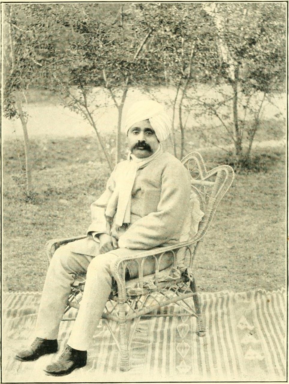 Old black-and-white photograph of Lala Lajpat Rai in a turban, sitting on a cane chair in a garden