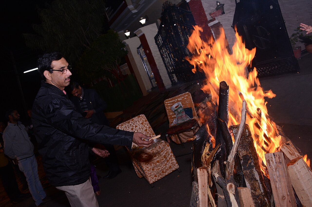 A man throws an offering into a blazing Lohri bonfire at night