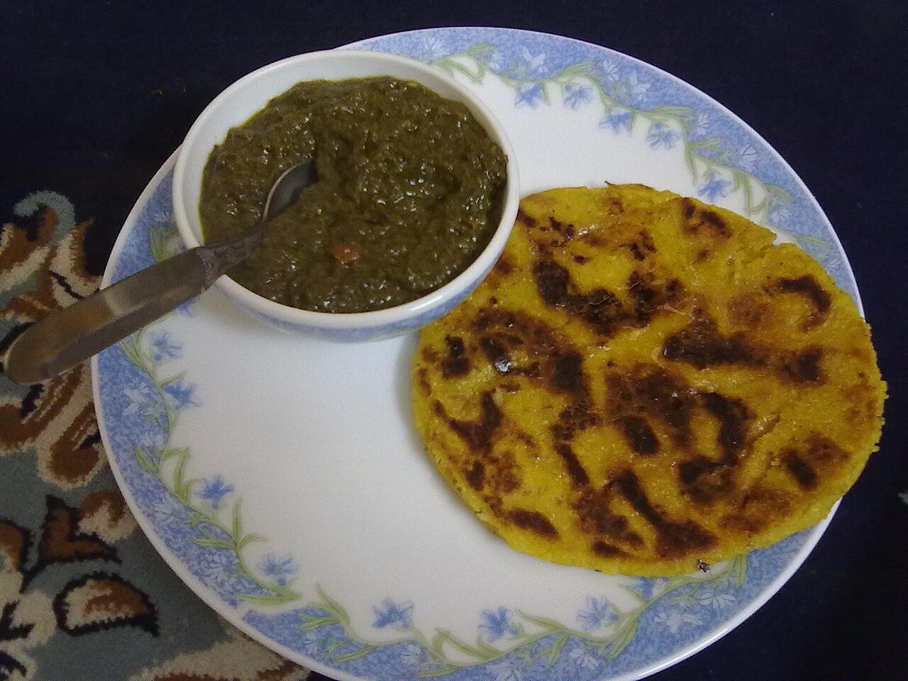 A bowl of green sarson da saag beside a yellow makki di roti on a plate