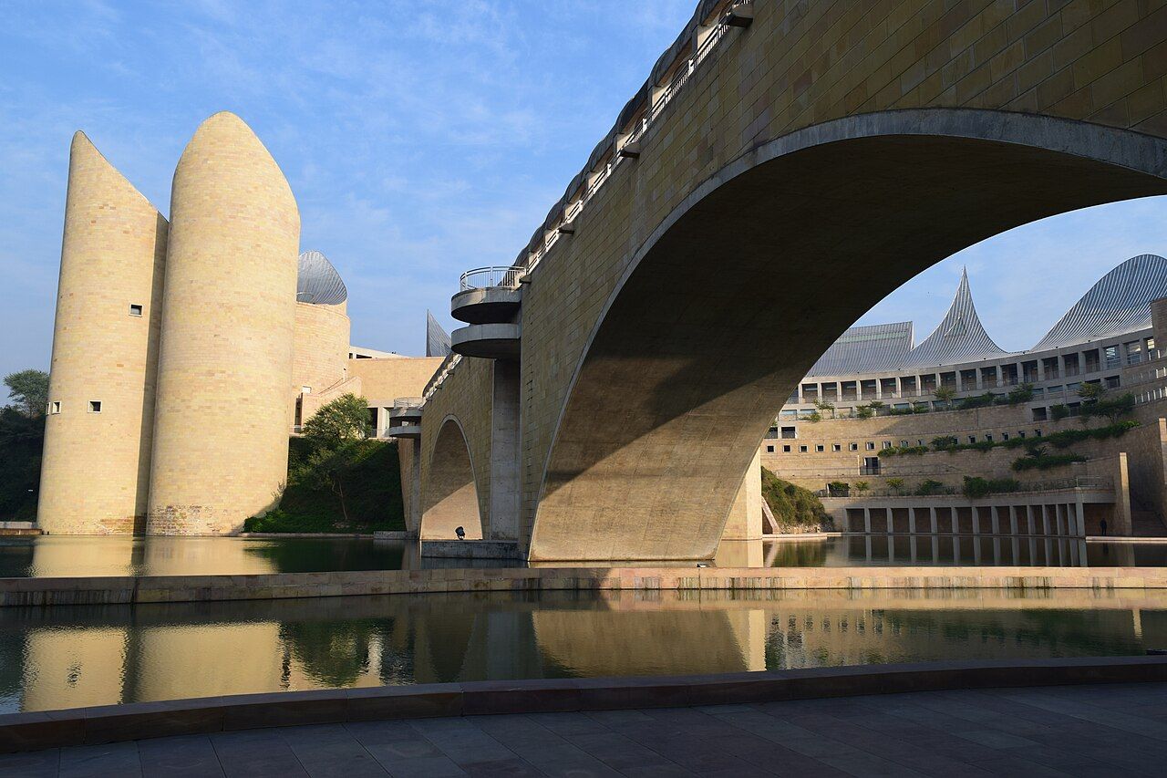 The sandstone towers, bridge and curved steel roofs of Virasat-e-Khalsa reflected in water