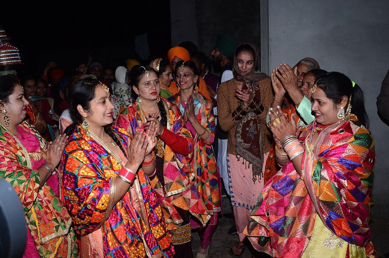 Smiling women in bright phulkari dupattas clapping together