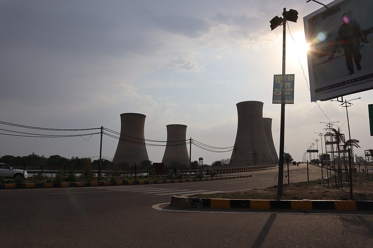 Four cooling towers of a power plant against the evening sky, beside a road