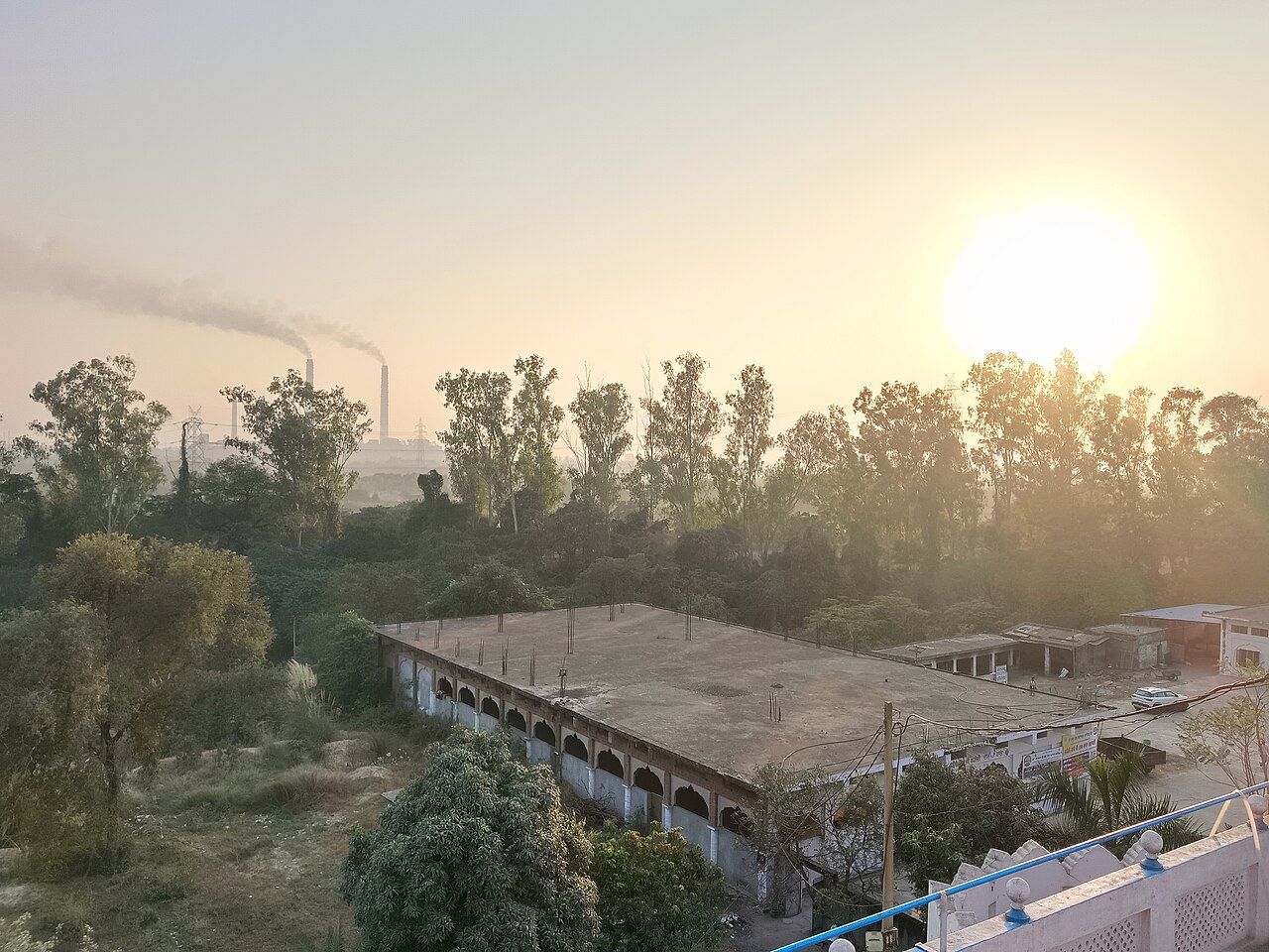 Two chimneys of a thermal power plant rising beyond trees at sunrise, Rupnagar