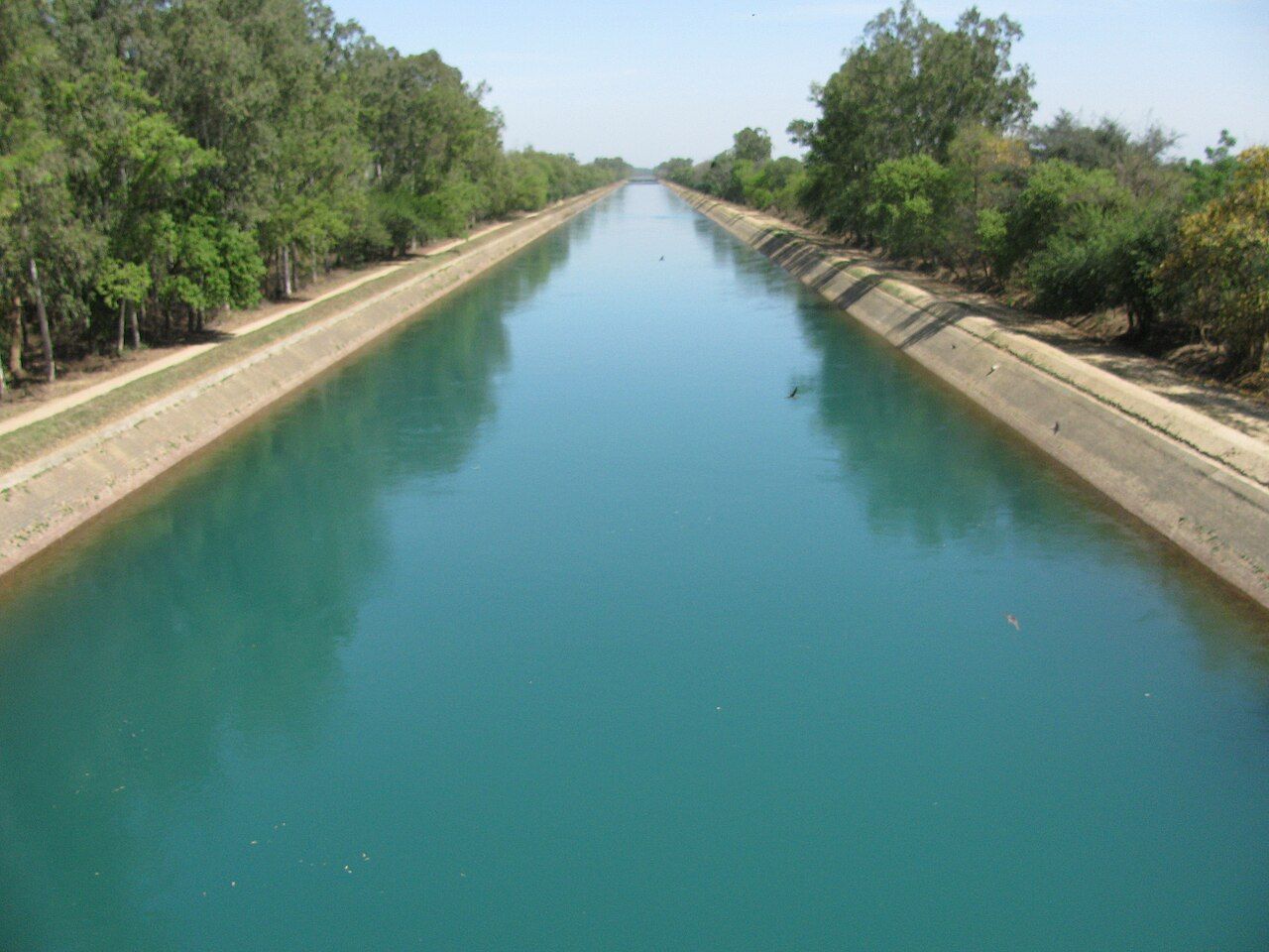 A straight, concrete-lined canal full of blue-green water between rows of trees