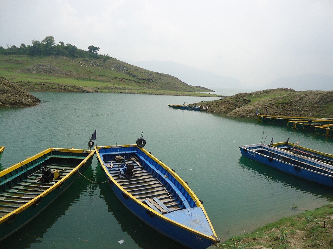Boats moored on the green water of Gobind Sagar lake among bare hills