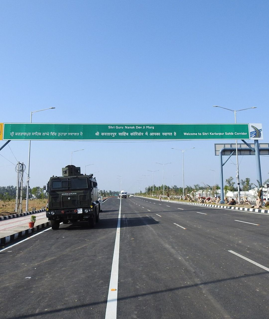 A wide new road with a green signboard at the entrance of the Kartarpur Corridor
