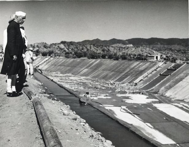 Black-and-white photo of Jawaharlal Nehru looking down into a large concrete-lined canal