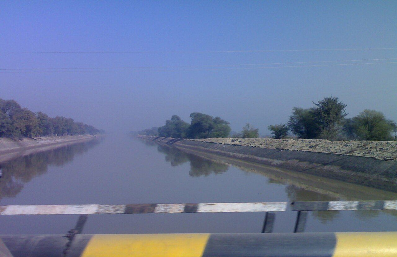 A wide, straight lined canal stretching to the horizon on a hazy morning, seen from a bridge railing