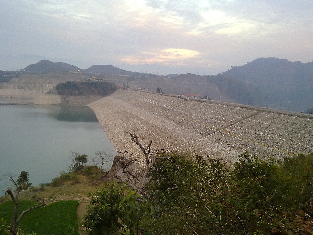 The long sloping wall of the Ranjit Sagar Dam with its reservoir on the left and hills behind