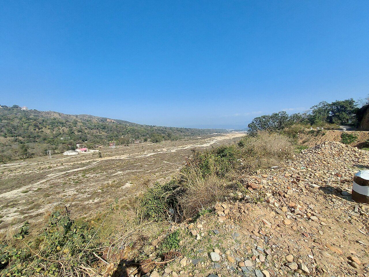 A wide, dry, stony stream bed with low wooded Shivalik hills beside it