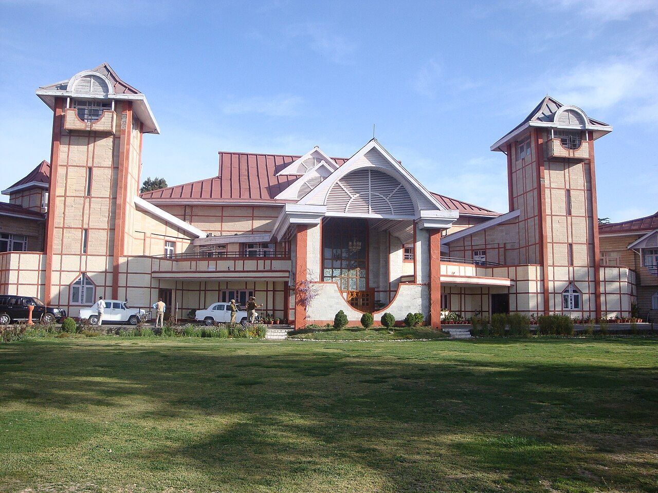 Large cream-and-red hill building with two towers and a lawn in front, Shimla