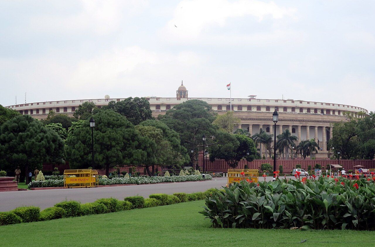Round colonnaded Parliament House in New Delhi behind trees and lawns