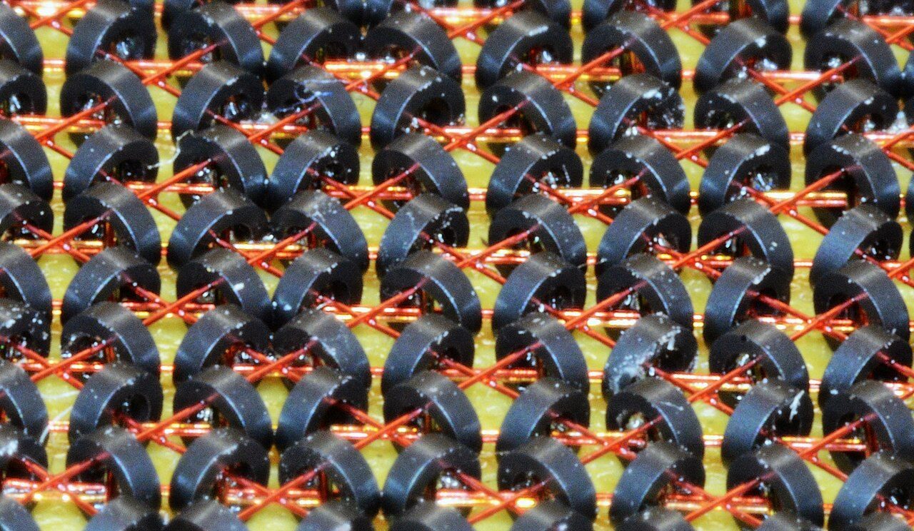 Close-up of a grid of tiny dark rings threaded on fine crossing wires: magnetic-core memory