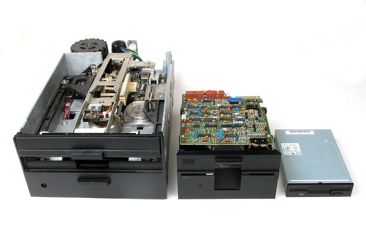 Three floppy disk drives side by side, from a large 8-inch drive to a small 3.5-inch drive